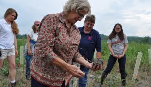 Women standing in farm field with one woman holding handful of soil