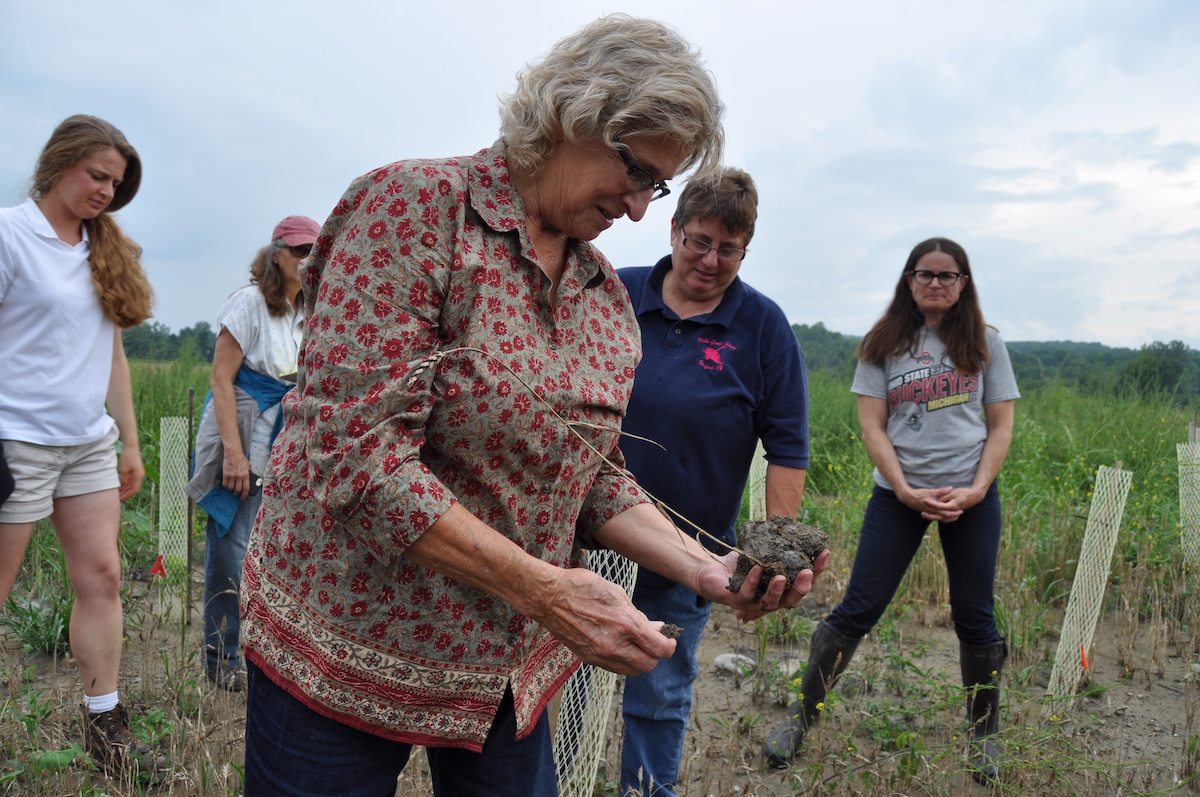 Women standing in farm field with one woman holding handful of soil