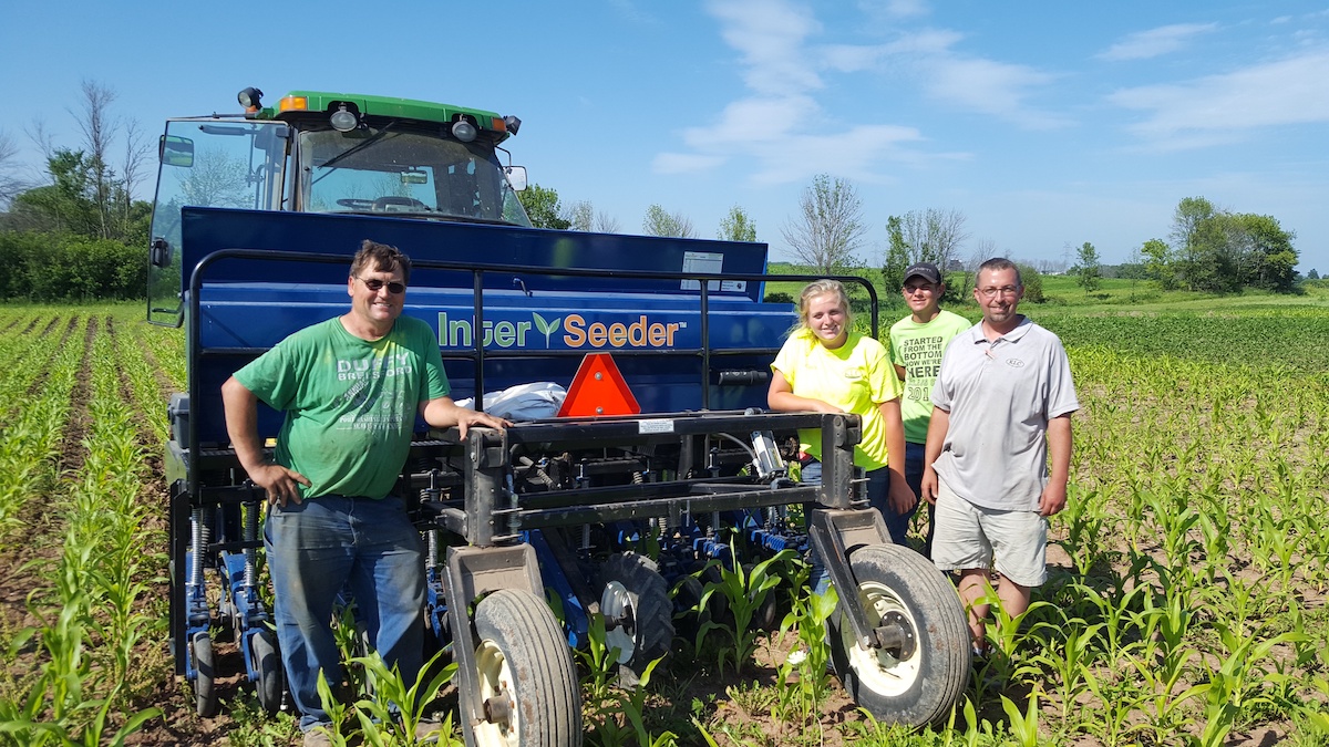 People standing around an interseeder in a farm field